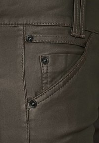 Hnědá džínovina s hladkým texturem, obsahující přední kapsu a detaily z černého kovu. Prošité okraje podtrhují design.