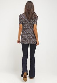 Krátký rukáv květinový tunik v tmavém vzoru s modrými, červenými a bílými květy; doplněný tmavými rozšířenými džíny a hnědými podpatky.