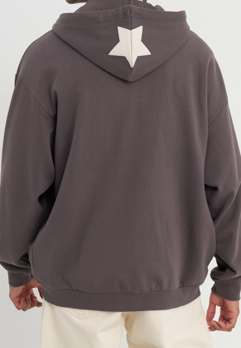 Sudadera con capucha en algodón gris oscuro, con un acento en forma de estrella blanca en la parte posterior de la capucha, puños de canalé y un corte holgado.