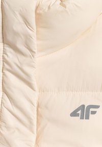 Tissu de veste matelassée couleur crème avec des coutures visibles et un logo réfléchissant "4F" sur le côté droit.