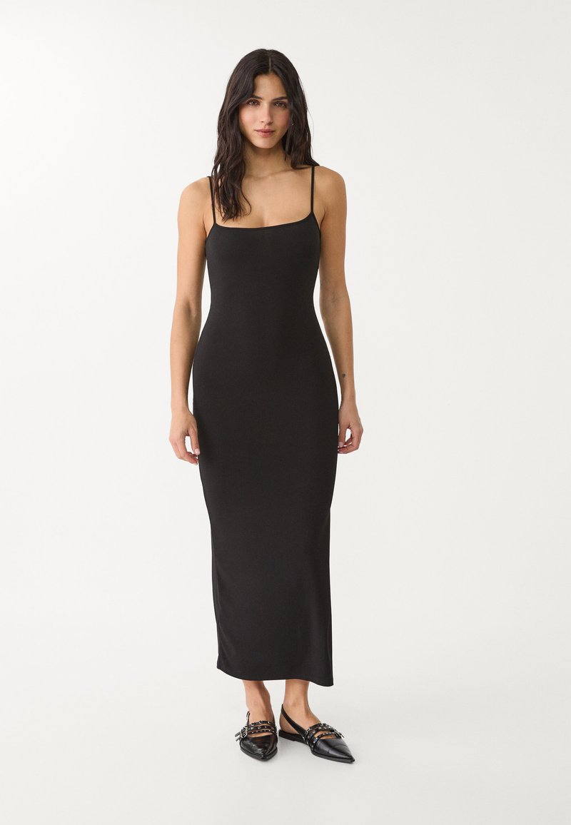 Robe maxi noire sans manches fabriquée en tissu doux, présentant une silhouette ajustée et un décolleté carré. Texture lisse sans motifs.