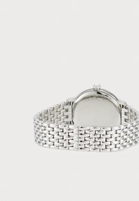 Silver metal watch with a woven bracelet design, round casing, and a prominent crown. Water-resistant up to 30 meters, minimalistic back.