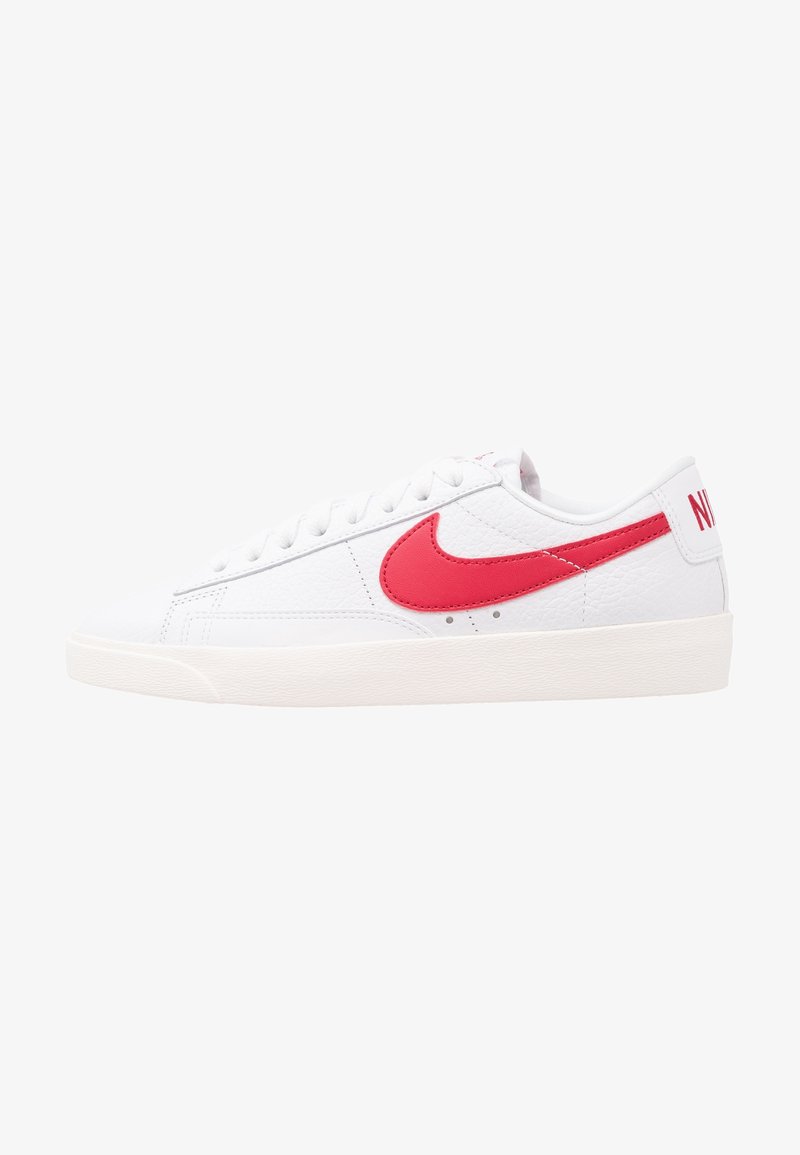 Bílé tenisky s texturovaným koženým svrškem, červeným logem swoosh a vypolstrovaným límcem. Vlastnosti zahrnují ploché šněrování a gumovou podrážku.