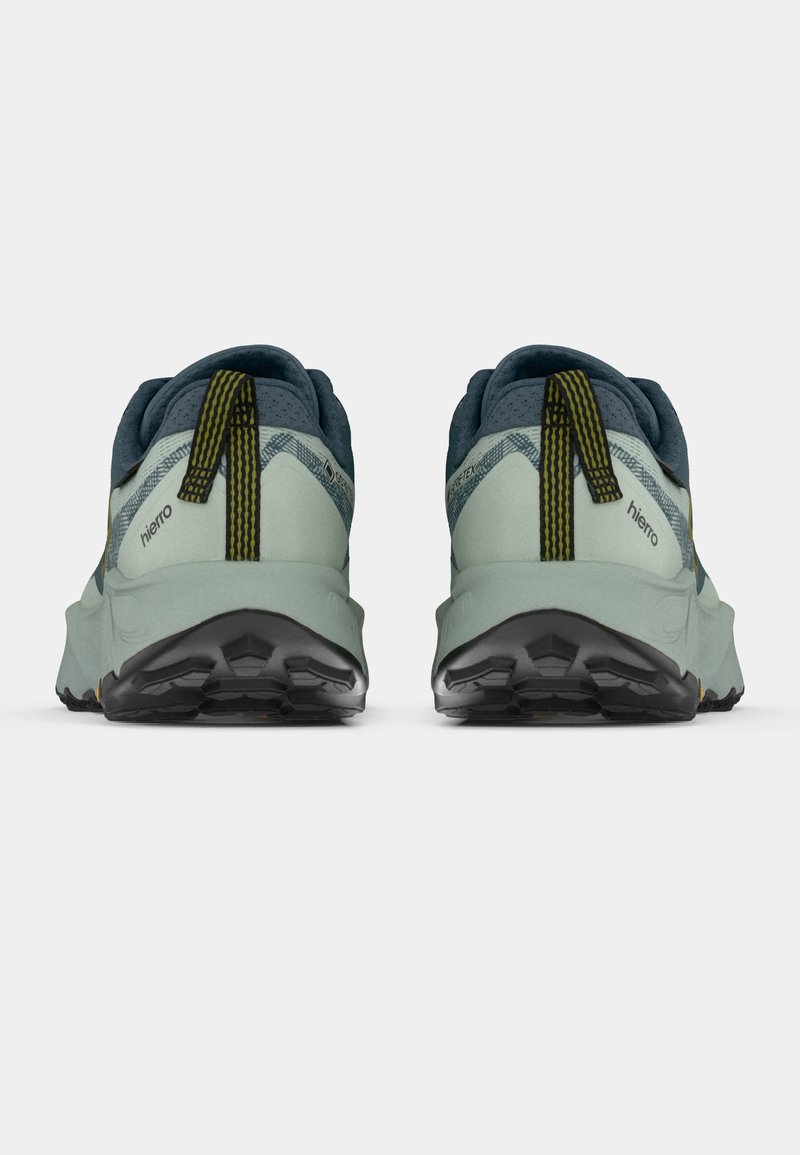 Running shoes with a light green upper, dark blue accents, textured mesh, and a rugged black sole. Features a prominent rear pull tab.