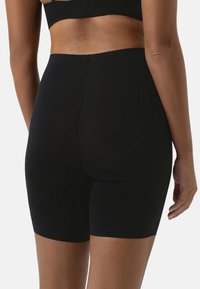 Svarta shapewear-shorts gjorda av stretchigt, slätt tyg. Har en medelhög midja och en sömlös design för komfort.
