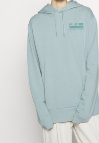 Sudadera azul claro hecha de una suave mezcla de algodón, que presenta un bolsillo tipo canguro, puños y dobladillo acanalados, y un pequeño gráfico en el pecho.