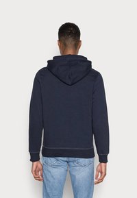 Tmavě modrá mikina s velkou kapucí, žebrovanými manžetami a spodním lemem. Vyrobena z měkké látky, s čistým, minimalistickým designem.