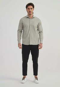 Chemise à boutons de couleur vert clair avec de fines rayures verticales, manches longues et col. Associée à un pantalon noir slim et des baskets blanches.