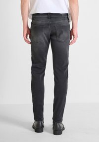 Vaqueros de denim negros ajustados con un acabado desgastado, cinco bolsillos y costuras en la parte trasera. Combinados con botas negras de tobillo.