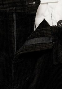 Gros plan sur un pantalon en velours côtelé noir avec une fermeture éclair, une sangle en velcro et une doublure intérieure matelassée blanche avec un bouton.