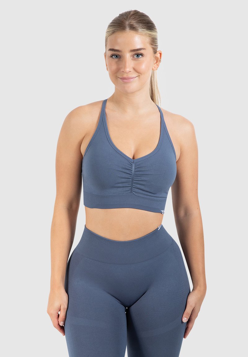 Sujetador deportivo azul con centro fruncido, tirantes ajustables, hecho de una tela elástica. Combinado con leggings azul a juego de alta cintura.