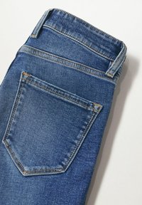 Pantalones vaqueros de mezclilla en azul medio con un acabado texturizado, que cuentan con un diseño de cinco bolsillos y un bolsillo tipo parche en la parte trasera con costuras en contraste.