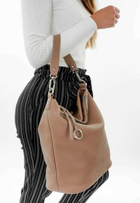 Sac à main en cuir tan au design décontracté, avec une fermeture éclair en métal argenté et un détail en métal circulaire. Porté sur un pantalon à rayures noires et blanches.