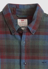 Kraag van een gebuttonde geruite shirt met rode, blauwe en groene patronen, met het Levi's-label binnenin de kraag.