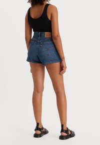 Denimshorts i medelblått med hög midja, med bakfickor och ett märkeslädermärke. Matchas med svarta sandaler.