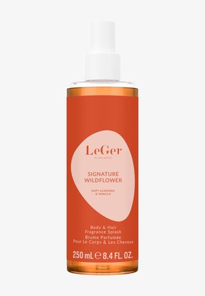 Botella de spray transparente con una etiqueta naranja que presenta un óvalo rosa claro. El texto indica un splash de fragancia para el cuerpo y el cabello con notas de almendra y vainilla.