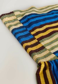 Gros plan sur une ceinture élastique sur un tissu à rayures horizontales dans des tons bleus, jaunes, verts et bruns.