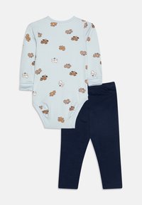 Otrodelna otroška oblačila, ki vključujejo svetlo modro bodi z dolgimi rokavi in motivi medvedkov ter temno mornarsko modre legice. Mehka tkanina, raztegljiv kroj.