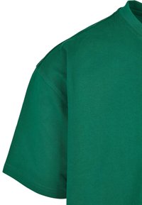 Zelené bavlněné tričko s kulatým výstřihem, krátkými rukávy a hladkou texturou. Tkanina má jemný žebrovaný vzor.