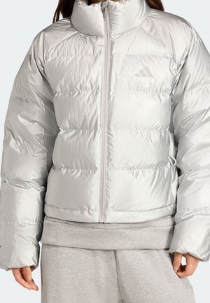 Femme portant une veste matelassée gris clair avec une fermeture éclair sur le devant et un col montant, associée à un pantalon de jogging gris clair.
