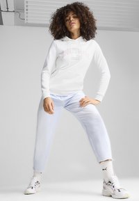 Sudadera blanca con el texto "SPORTSWEAR" en rosa, combinada con jeans azul claro y zapatillas blancas con acentos multicolores. Texturas de tela suaves.