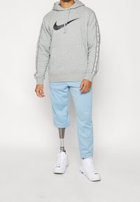 Grå huvtröja med svart Nike-logotyp, med vita randig detaljer. Ljust blå byxor, kompletterade med vita sportskor. Protesben synligt.