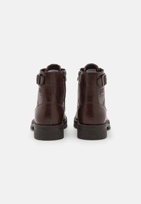 Botas de tobillo de cuero marrón con un acabado suave, que presentan un cierre lateral con cremallera, detalle de hebilla y una resistente suela de goma negra.