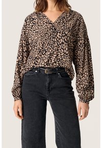 Blusa a maniche lunghe in nero e beige con motivo astratto, caratterizzata da scollo a V, bottoni sul davanti e polsini arricciati, abbinata a jeans neri a vita alta.
