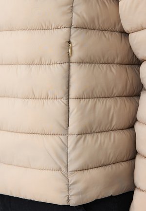 Beige Pufferjacke mit gestepptem Muster, horizontalen Nähten und einem goldenen Reißverschlussdetail an der Seite. Weiches, leichtes Material.
