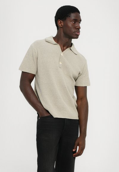 Μπεζ κοντομάνικο πόλο μπλουζάκι με υφασμάτινη υφή, κολάρο και ξύλινους κουμπιά, σε συνδυασμό με μαύρα τζιν.