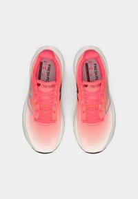 Une paire de chaussures de course New Balance Fresh Foam 1080 brillantes en rose et blanc, vues du dessus sur un fond uni.