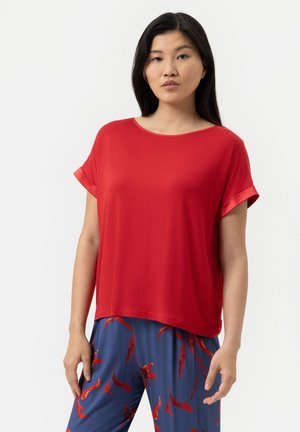 Top corto rojo de manga corta con un escote amplio y un corte relajado. Textura suave, tela ligera. Combinado con pantalones azules que presentan un patrón floral rojo.