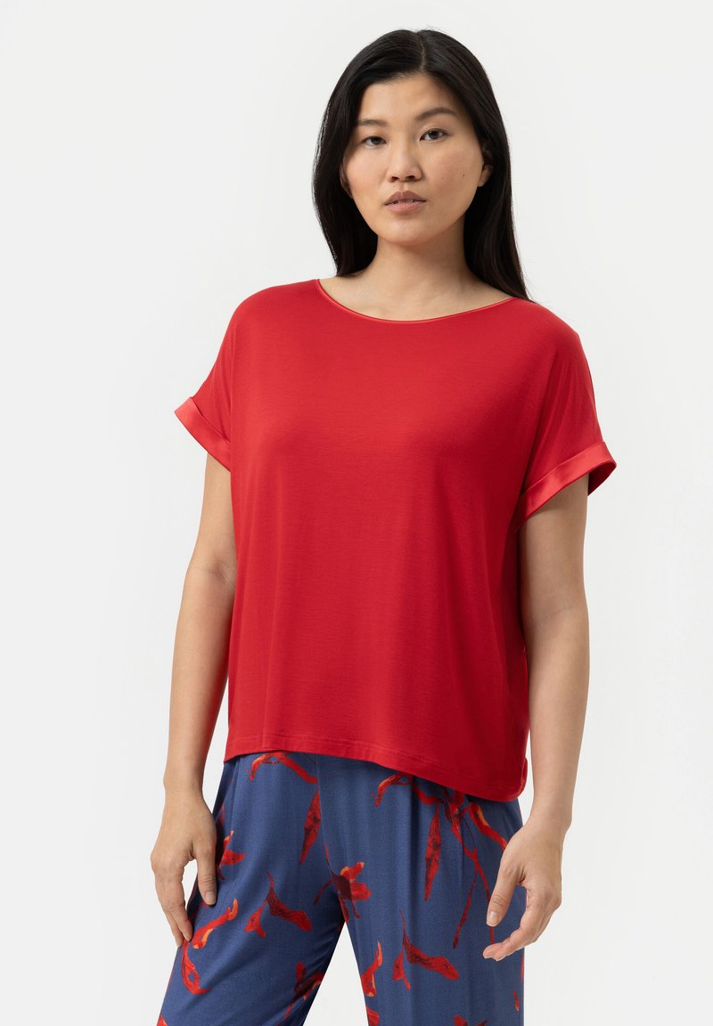 Röd topp med korta ärmar, vid halsringning och avslappnad passform. Slät textur, lättviktsmaterial. Kombinerad med blå byxor med ett rött blommönster.