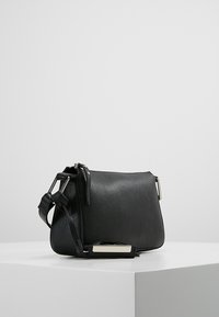 Black textured leather crossbody bag with adjustable strap and silver rectangular metal accent, placed on a white pedestal against a plain background.