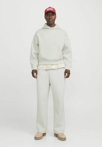 Hanorac gri deschis și pantaloni asortați dintr-un material moale. Căciulă roșie cu text alb. Pantofi bej. Aspect general casual, relaxat, cu un look în straturi.