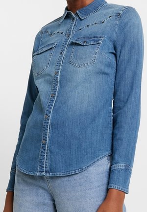 Blauw denim overhemd met lange mouwen, drukknoopsluiting, twee borstzakken en subtiele stikdetails over de bovenborst.