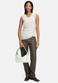Biała bezrękawnikowa bluzka z teksturowanej tkaniny, oliwkowe spodnie o prostym kroju oraz biała skórzana torebka z czarnymi akcentami. Czarne buty.