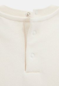 Top in maglia di colore crema chiaro con scollatura rotonda, tre chiusure a pressione sul retro e texture a coste.