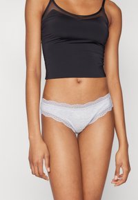 Graue Baumwollslips mit zarter Spitze. Kombiniert mit einem schwarzen, figurbetonten Tanktop, das einen durchsichtigen Mesh-Bereich am Ausschnitt hat.