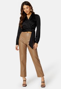 Top avvolgente in satin nero con maniche lunghe e cintura in vita, abbinato a pantaloni in pelle sintetica color cammello a vita alta e tacchi neri con strappi.