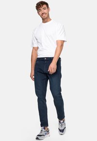 Donkerblauwe denim jeans met een slim fit, voorzien van een knoop- en ritssluiting, een klassiek vijf-pocket ontwerp en een wit katoenen t-shirt.