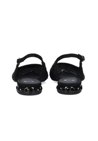 Sandalias negras con parte superior texturizada, correa ajustable en el tobillo y acentos decorativos de cuentas en la suela. Diseño plano para mayor comodidad.