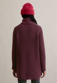 Gebreide paarse trui met een hoge kraag, textuurstof en lange mouwen. Gecombineerd met een felroze, donzige beanie.