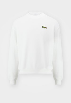 Hanorac alb cu guler rotund, având un mic logo brodat de crocodil verde pe partea stângă a pieptului și mansete și tiv din tricot.