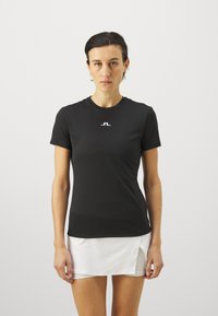 Juodas sportinis marškinėlis trumpomis rankovėmis ir apvaliu kaklu, su baltu logotipu krūtinėje. Lygus, lengvas audinys.