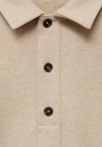 Camicia in misto lana beige con colletto classico, cinque bottoni neri e finitura testurizzata. Include un dettaglio della tasca sul petto.