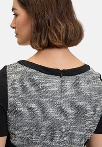 Schwarz-weißes Kleid mit einem strukturierten Strickrücken, einem schwarzen Ausschnitt und einem Reißverschluss hinten. Kurze Ärmel und taillierter Schnitt.