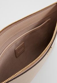 Béžové kožené pouzdro se zlatým zipem, zobrazující hladký látkový vnitřek a malou přišitou vnitřní kapsu.