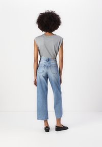 Camiseta cinza sem mangas combinada com jeans de perna reta de cintura alta, azul claro. Apresenta cinco bolsos e um efeito desgastado. Sapatos planos pretos.