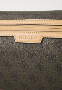 Matériau synthétique noir texturé avec des accents en cuir beige clair. Présente un logo embossé et des détails cousus à l'avant.